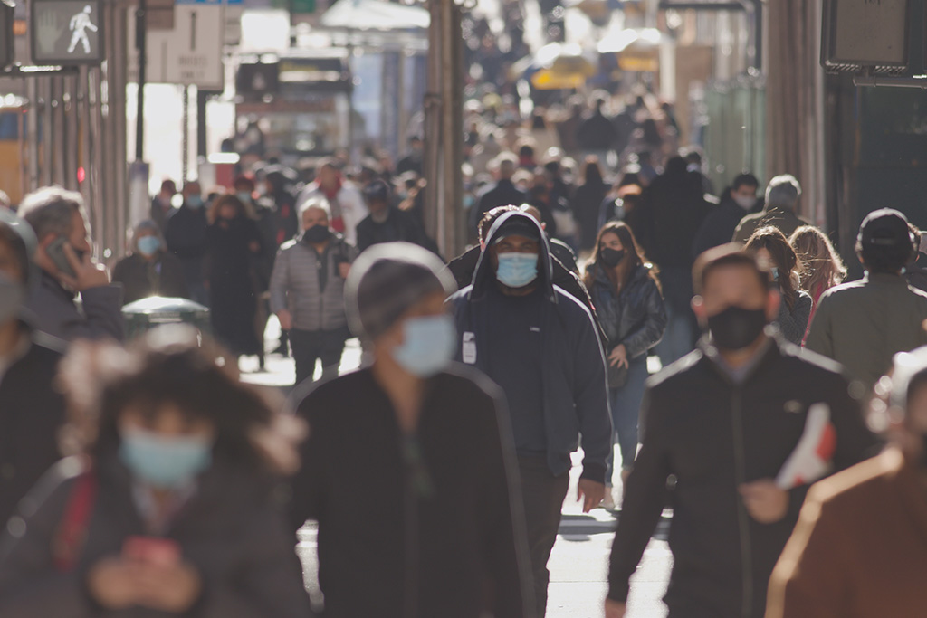 Peatones caminando por la ciudad, vistos de frente y usando mascarillas